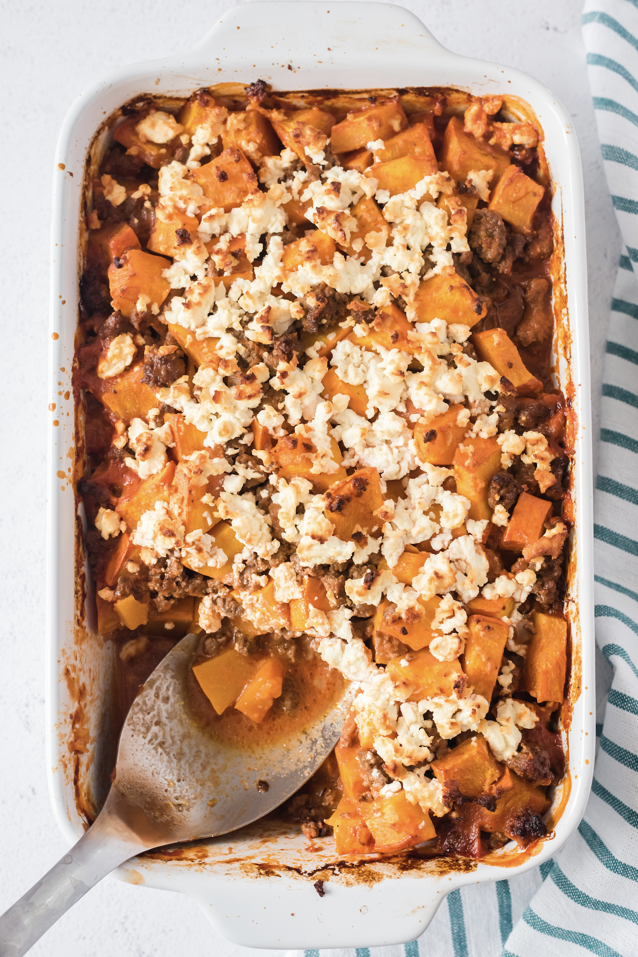 A pumpkin ground beef casserole in a white casserole dish with a large serving spoon