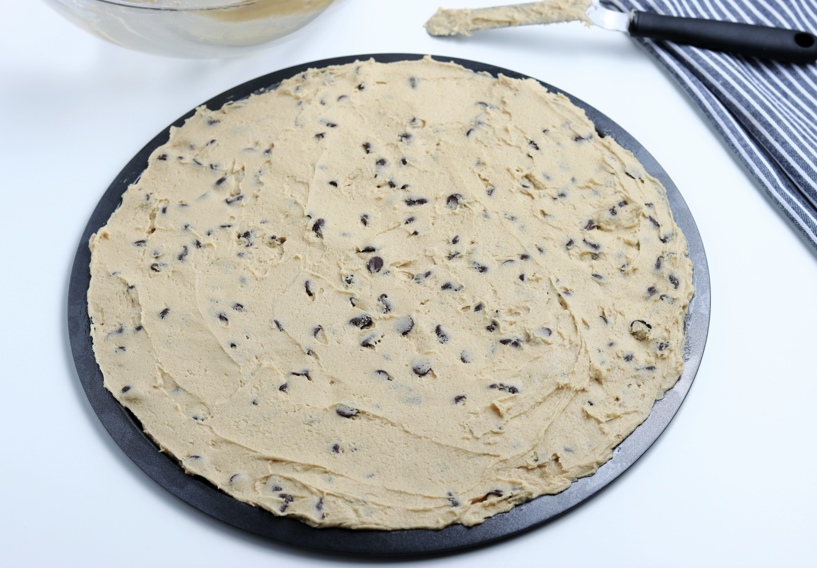 Spreading the chocolate chip cookie dough on a round pizza tray