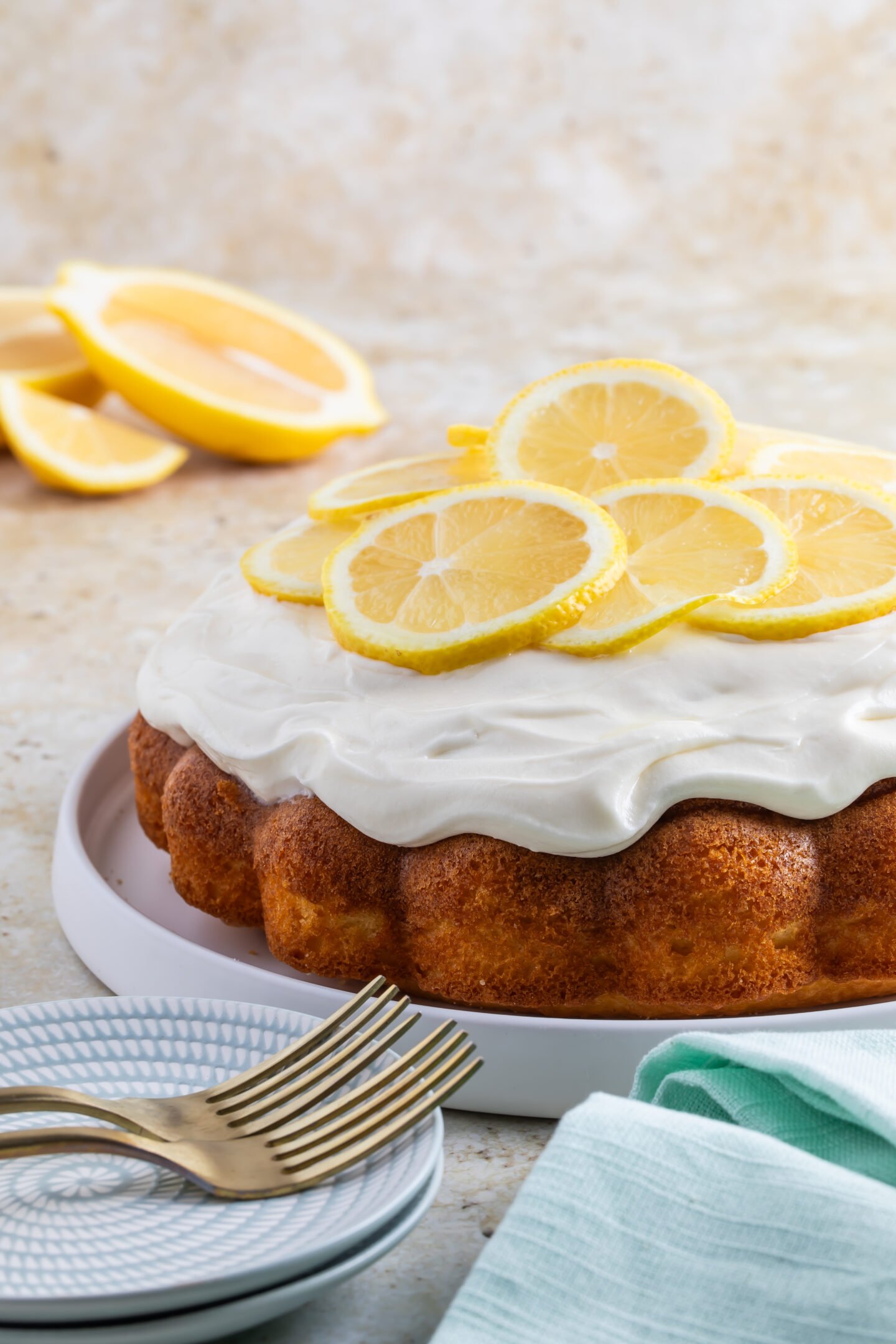 Classic cream cheese frosting spread onto bundt cake with sliced lemons 