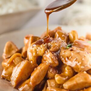 Teriyaki sauce being drizzled over cashew chicken with tender chicken pieces and crunchy cashews i