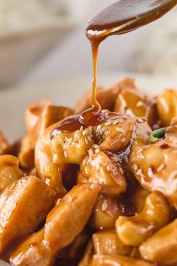 Teriyaki sauce being drizzled over cashew chicken with tender chicken pieces and crunchy cashews i