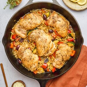 One pan Mediterranean chicken and couscous in a skillet with juicy chicken thighs, pearl couscous, vegetables, olives, and fresh herbs