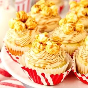 Caramel Popcorn Cupcakes arranged on a white platter, topped with buttery caramel popcorn and caramel drizzle