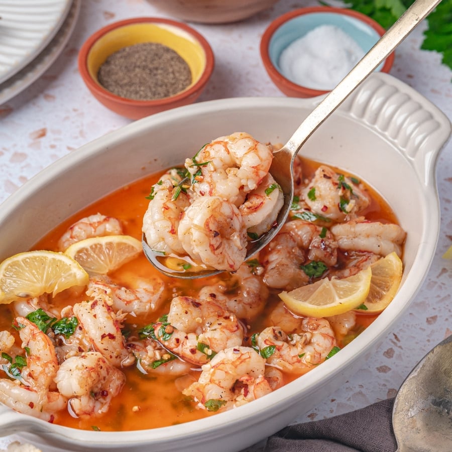 garlic butter shrimp served in white bowl with parsley and lemon