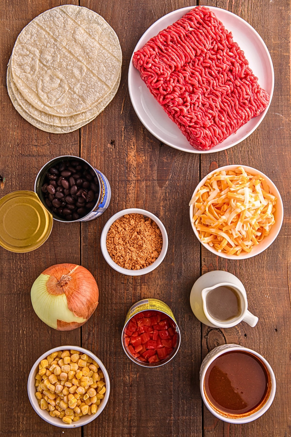 ingredients for Mexican casserole including ground beef tortillas cheese beans corn and enchilada sauce