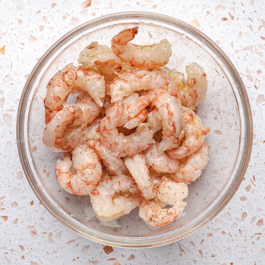 seasoning shrimp with olive oil salt and pepper before cooking