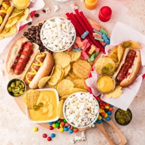 Ultimate movie night snack board with hot dogs, popcorn, potato chips, cheese dip, candy, and chocolate arranged on a large wooden serving tray