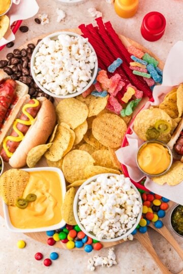 Ultimate movie night snack board with hot dogs, popcorn, potato chips, cheese dip, candy, and chocolate arranged on a large wooden serving tray