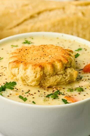 Creamy Chicken Pot Pie Soup with shredded chicken, carrots, celery and peas served in a bowl with a warm buttermilk biscuit
