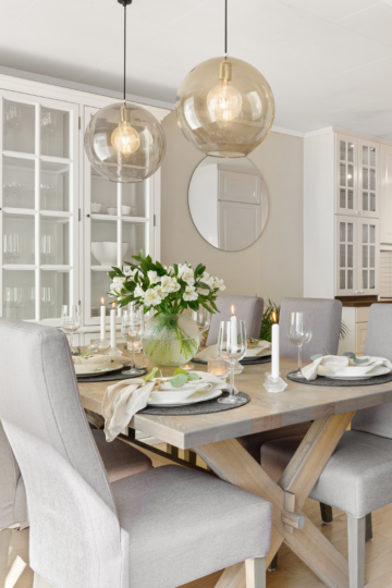 Functional dining room with a wooden table, gray upholstered chairs, glass pendant lights, and white display cabinets.