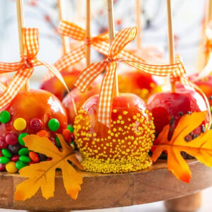 Mini caramel apples on wooden sticks decorated with fall-colored sprinkles and mini M&M's.
