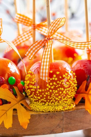 Mini caramel apples on wooden sticks decorated with fall-colored sprinkles and mini M&M’s.